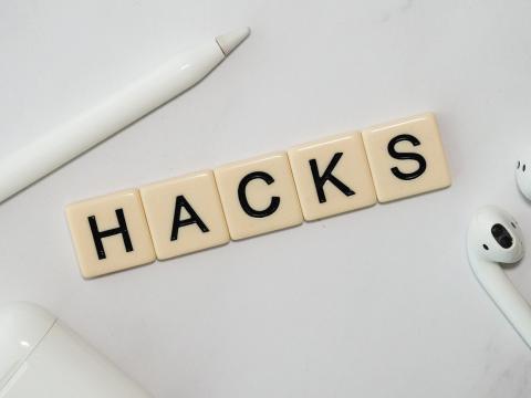Dominosteine die das Wort Hacks zeigen, ein Stift und Earpods